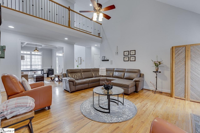 living room featuring ceiling fan, ornamental molding, light hardwood / wood-style flooring, and a towering ceiling