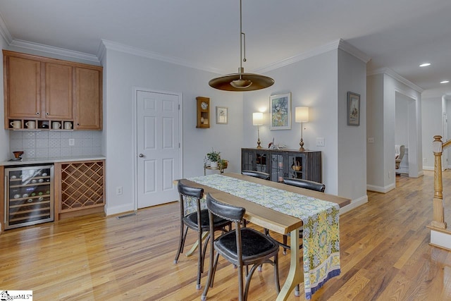 dining area with crown molding, bar, beverage cooler, and light wood-type flooring