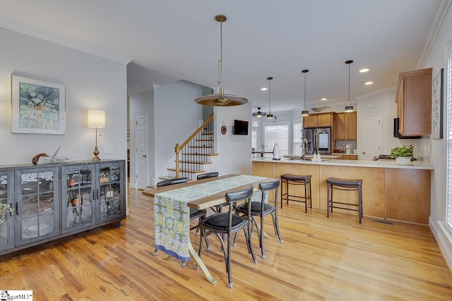 kitchen with crown molding, stainless steel fridge, kitchen peninsula, and light wood-type flooring