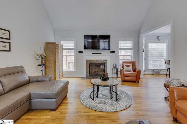 living room featuring a high end fireplace, vaulted ceiling, a healthy amount of sunlight, and light wood-type flooring