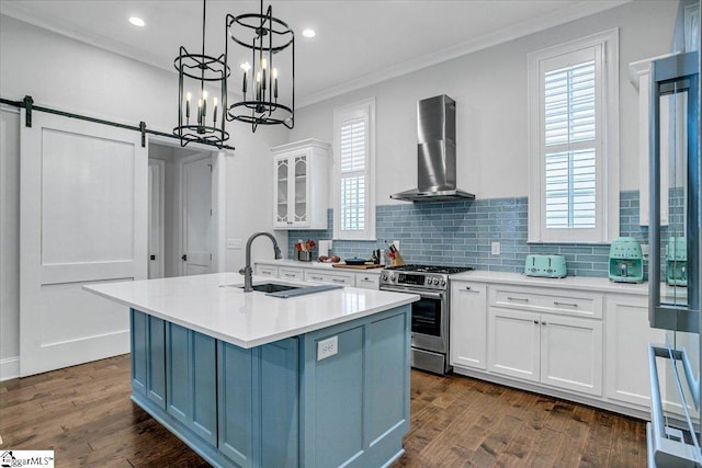 kitchen featuring white cabinetry, sink, stainless steel range with gas stovetop, a center island with sink, and wall chimney range hood