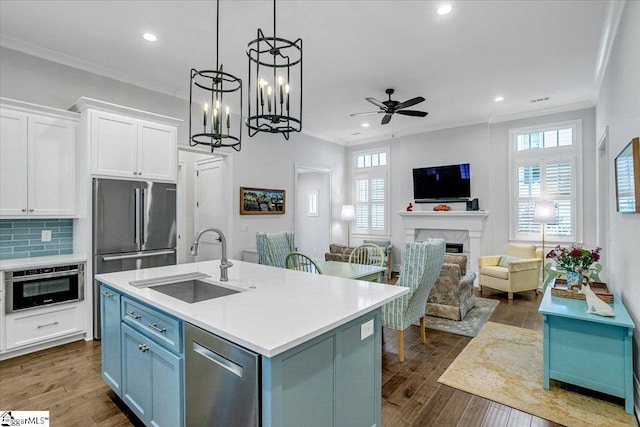 kitchen with sink, a kitchen island with sink, stainless steel appliances, a high end fireplace, and white cabinets