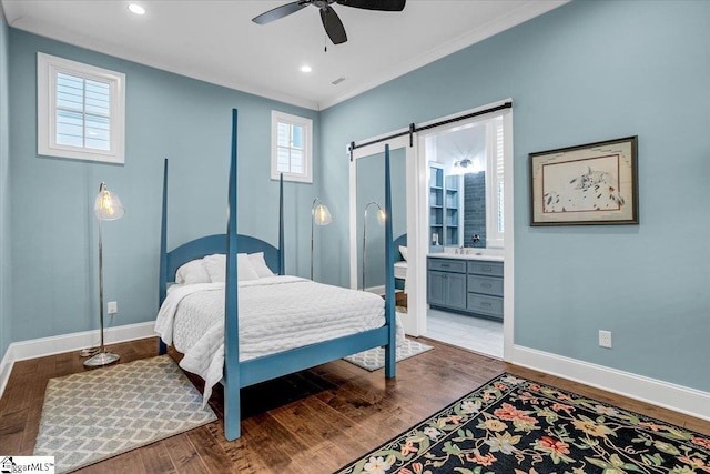 bedroom featuring ensuite bathroom, hardwood / wood-style flooring, ornamental molding, ceiling fan, and a barn door