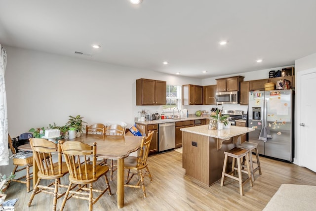 kitchen with sink, a breakfast bar area, a kitchen island, stainless steel appliances, and light hardwood / wood-style floors