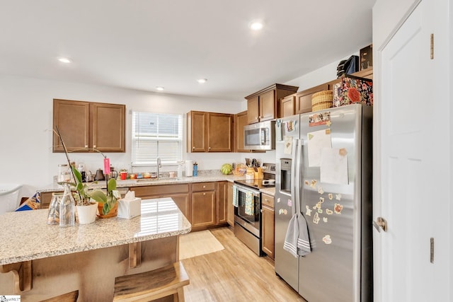 kitchen with sink, light stone counters, light hardwood / wood-style flooring, a kitchen breakfast bar, and stainless steel appliances