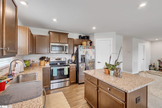 kitchen with sink, light hardwood / wood-style flooring, a kitchen island, stainless steel appliances, and light stone countertops