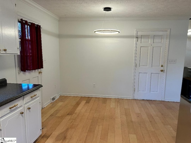 unfurnished dining area featuring ornamental molding, a textured ceiling, and light hardwood / wood-style floors