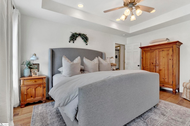 bedroom with a raised ceiling, light wood-type flooring, and ceiling fan