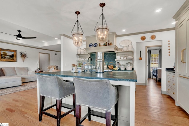 kitchen with pendant lighting, a kitchen bar, ornamental molding, ceiling fan, and light wood-type flooring