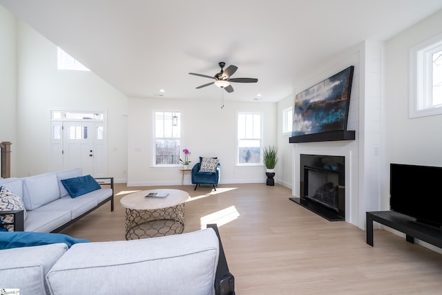 living room featuring a large fireplace, ceiling fan, and light wood-type flooring