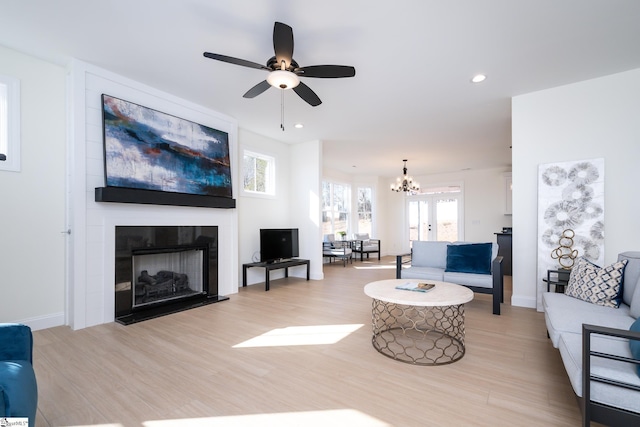 living room with a large fireplace, ceiling fan with notable chandelier, and light hardwood / wood-style floors