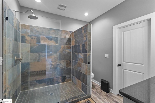 bathroom with hardwood / wood-style floors, toilet, and tiled shower