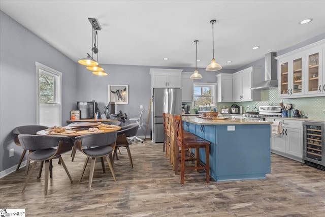 kitchen with appliances with stainless steel finishes, white cabinetry, wine cooler, a center island, and wall chimney range hood