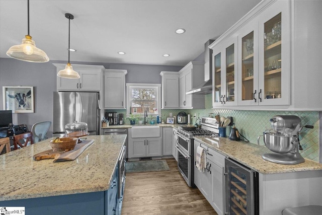 kitchen featuring sink, beverage cooler, hanging light fixtures, stainless steel appliances, and wall chimney exhaust hood