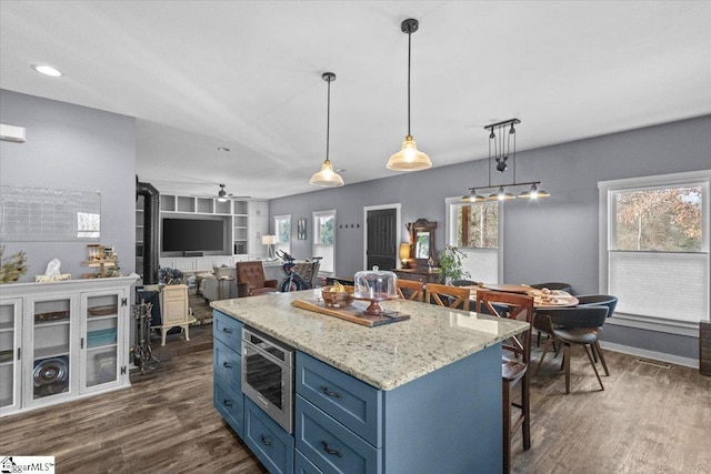 kitchen featuring blue cabinetry, built in shelves, a wood stove, stainless steel microwave, and pendant lighting