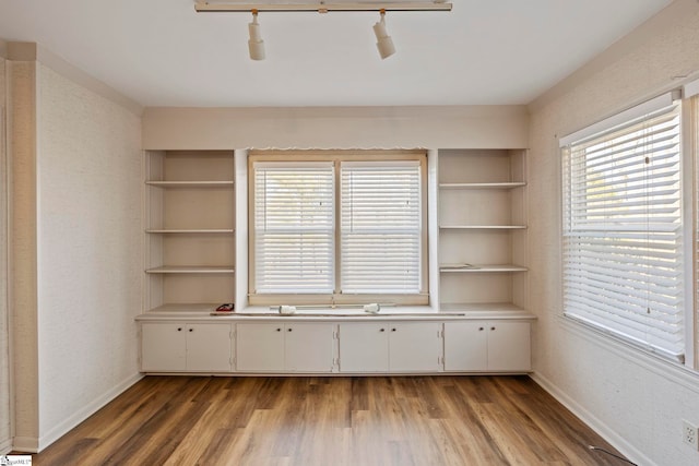 interior space with built in shelves, plenty of natural light, rail lighting, and wood-type flooring