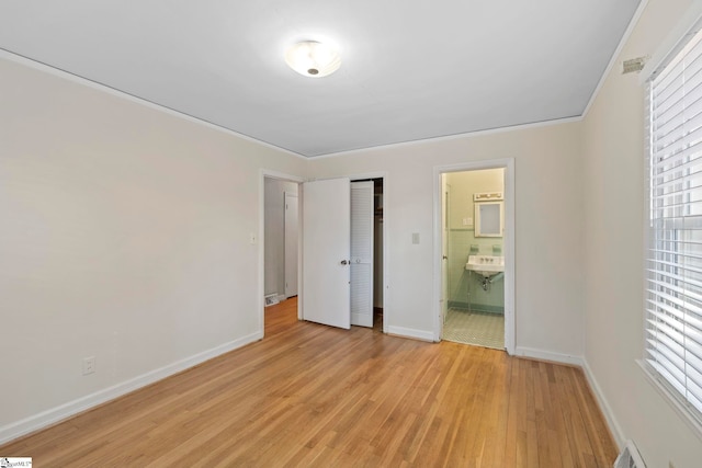 unfurnished bedroom featuring multiple windows, connected bathroom, light hardwood / wood-style floors, and a closet