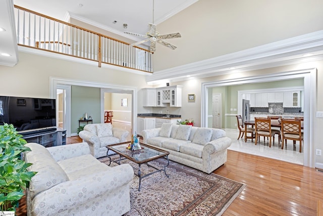 living room with crown molding, a towering ceiling, ceiling fan, and hardwood / wood-style flooring