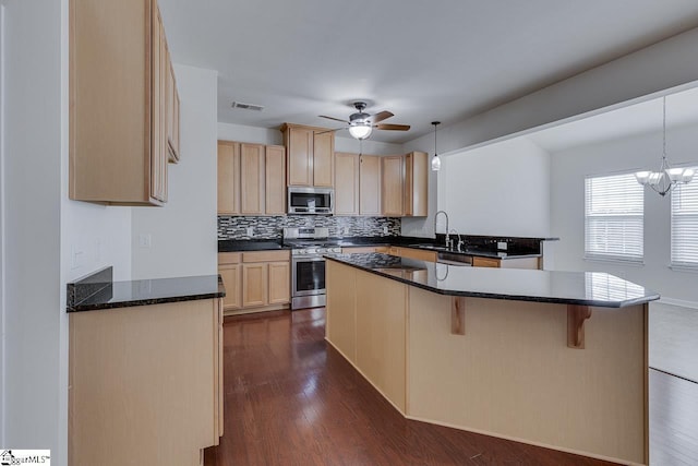 kitchen featuring dark wood-type flooring, hanging light fixtures, light brown cabinets, stainless steel appliances, and ceiling fan with notable chandelier