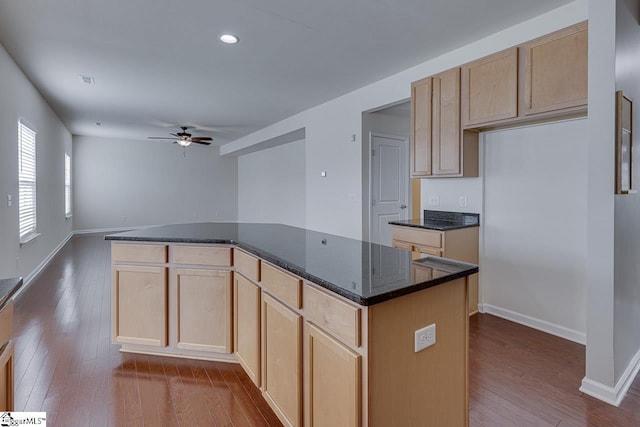 kitchen featuring a kitchen island, hardwood / wood-style floors, light brown cabinetry, dark stone countertops, and ceiling fan