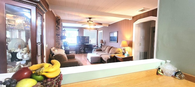 living room with ceiling fan, wooden walls, and beam ceiling