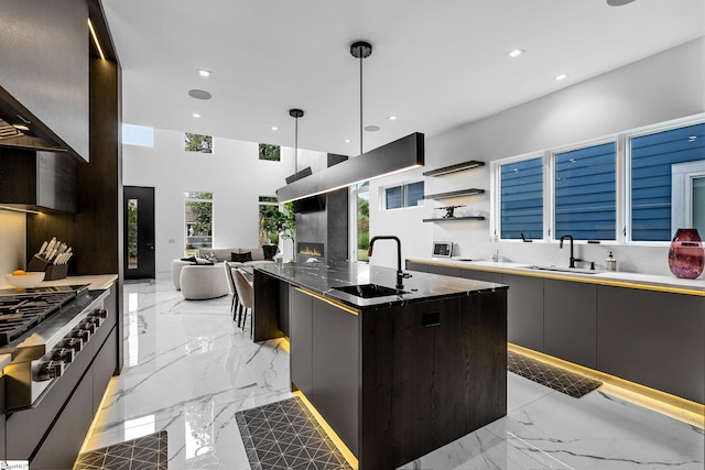 kitchen with wall chimney exhaust hood, cooktop, sink, decorative light fixtures, and a center island