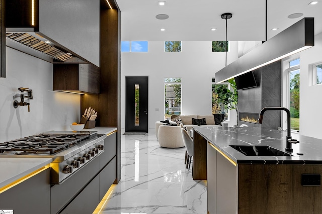 kitchen featuring stainless steel gas cooktop, sink, hanging light fixtures, dark stone countertops, and a fireplace