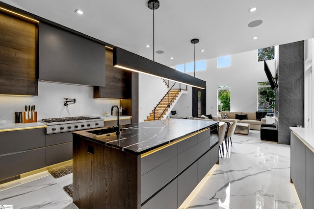 kitchen featuring pendant lighting, sink, a kitchen island with sink, backsplash, and stainless steel gas stovetop