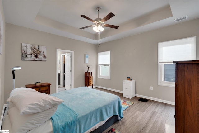 bedroom with a tray ceiling, light hardwood / wood-style floors, ceiling fan, and ensuite bathroom