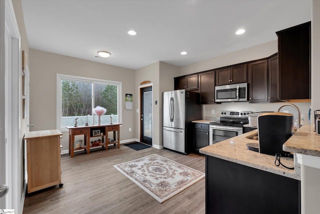 kitchen featuring light stone counters, dark brown cabinetry, light hardwood / wood-style floors, and appliances with stainless steel finishes