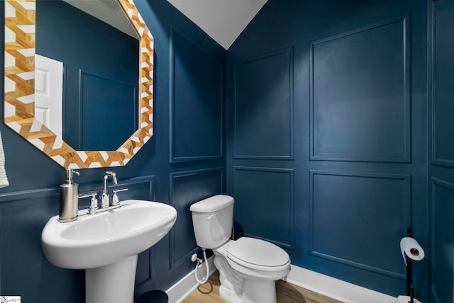 bathroom with hardwood / wood-style floors, vaulted ceiling, sink, and toilet