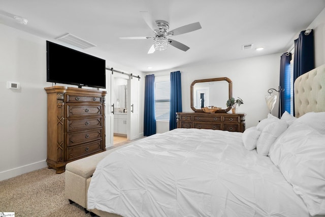 bedroom with ceiling fan, connected bathroom, a barn door, and light carpet