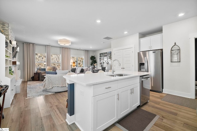 kitchen with sink, white cabinetry, light wood-type flooring, an island with sink, and stainless steel appliances