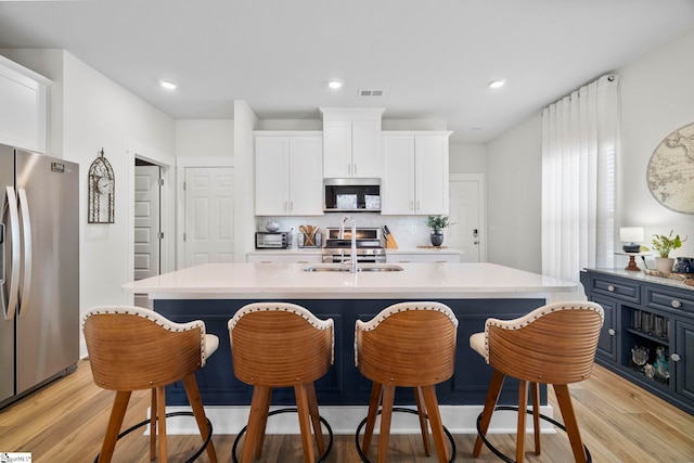 kitchen featuring a kitchen island with sink, sink, white cabinets, and appliances with stainless steel finishes