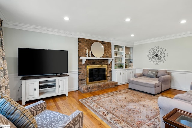 living room featuring crown molding, built in shelves, a brick fireplace, and light wood-type flooring