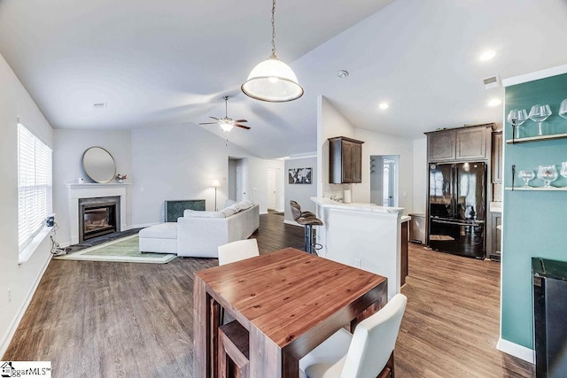 dining room featuring visible vents, a ceiling fan, wood finished floors, vaulted ceiling, and a high end fireplace