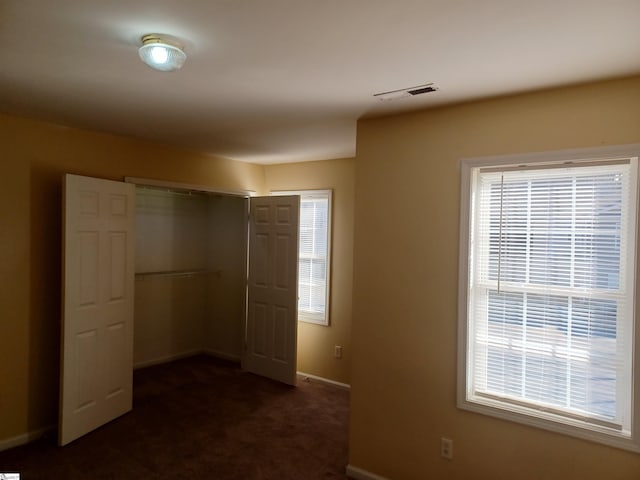 unfurnished bedroom with dark carpet and a closet