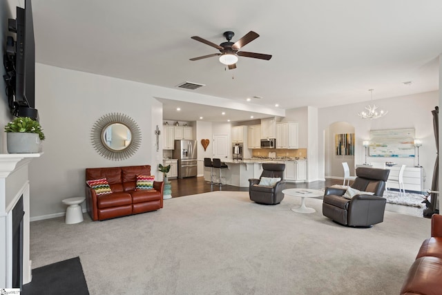 living room with ceiling fan with notable chandelier and dark carpet