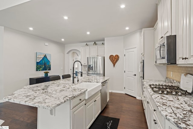 kitchen featuring sink, appliances with stainless steel finishes, backsplash, white cabinets, and a center island with sink