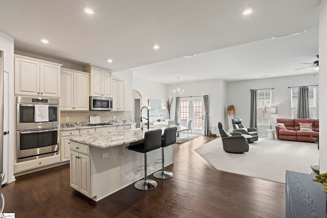 kitchen featuring appliances with stainless steel finishes, a kitchen bar, a kitchen island with sink, light stone counters, and dark wood-type flooring