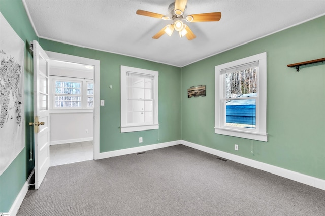 carpeted spare room with ceiling fan, a healthy amount of sunlight, and a textured ceiling