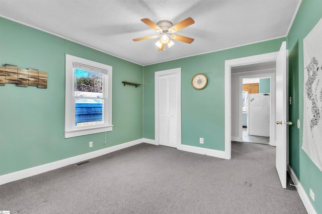 unfurnished bedroom with a textured ceiling, white refrigerator, a closet, ceiling fan, and carpet