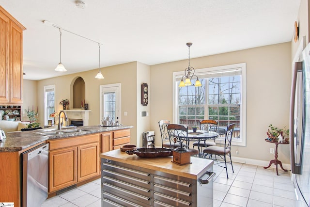 kitchen featuring light tile patterned flooring, sink, hanging light fixtures, appliances with stainless steel finishes, and dark stone counters