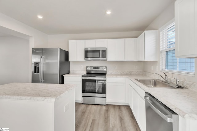 kitchen with appliances with stainless steel finishes, sink, white cabinets, a center island, and light hardwood / wood-style floors