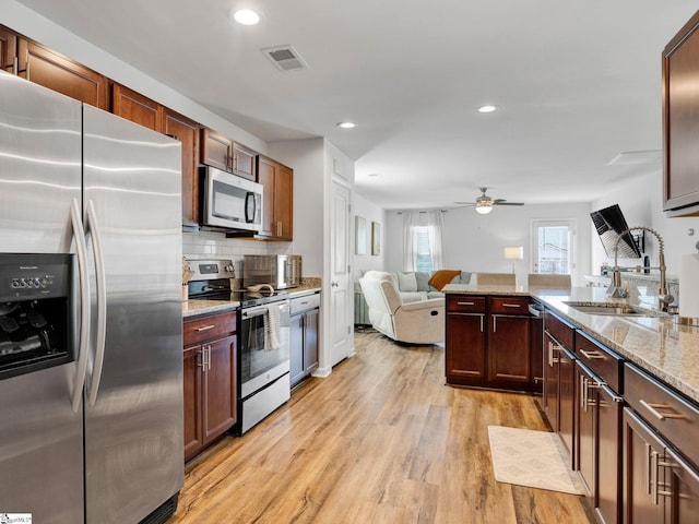 kitchen featuring sink, light hardwood / wood-style flooring, stainless steel appliances, tasteful backsplash, and light stone countertops