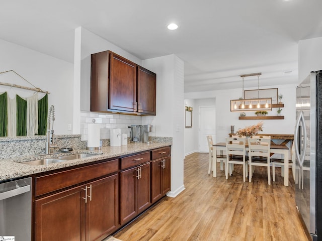 kitchen featuring tasteful backsplash, sink, hanging light fixtures, stainless steel appliances, and light stone countertops