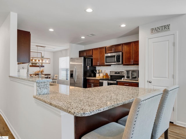 kitchen featuring appliances with stainless steel finishes, hanging light fixtures, a kitchen breakfast bar, light stone counters, and kitchen peninsula