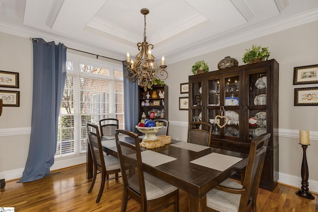 dining room with a raised ceiling, ornamental molding, dark wood-type flooring, and an inviting chandelier