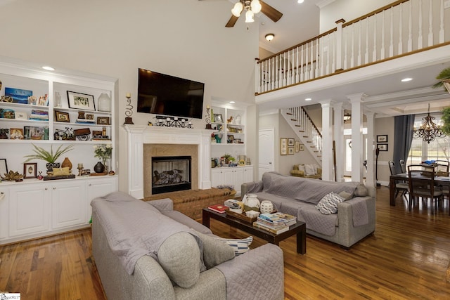 living room with a high ceiling, ornamental molding, dark wood-type flooring, and ceiling fan with notable chandelier