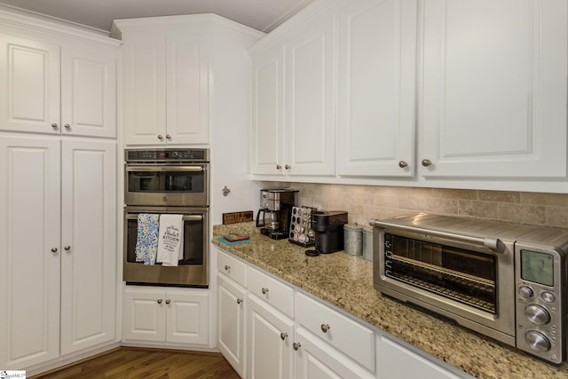 kitchen with hardwood / wood-style flooring, stainless steel double oven, white cabinets, and backsplash